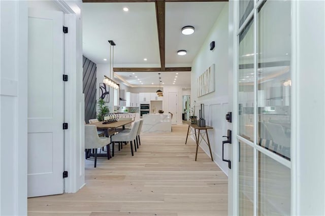 hall with light wood finished floors, beamed ceiling, and recessed lighting