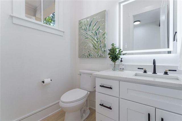 bathroom with toilet, vanity, wood finished floors, and baseboards