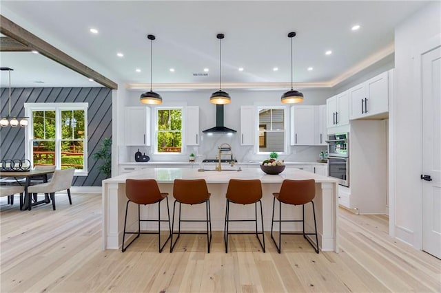 kitchen with wall chimney exhaust hood, light countertops, white cabinetry, light wood-style flooring, and recessed lighting