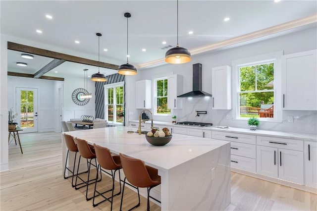 kitchen featuring wall chimney range hood, tasteful backsplash, stainless steel gas stovetop, light wood-style floors, and recessed lighting