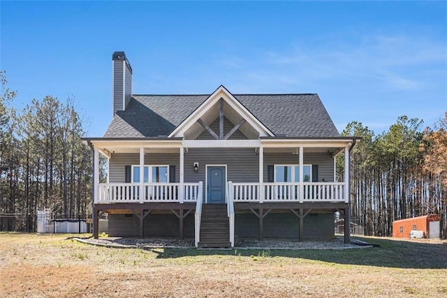 view of front of property with covered porch, a front lawn, a shingled roof, and a chimney