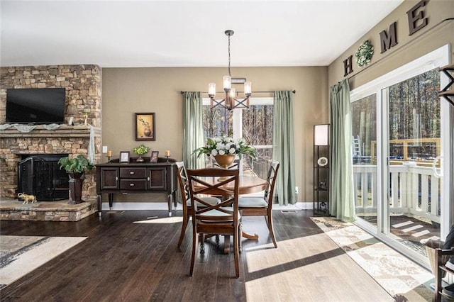 dining area with baseboards, a stone fireplace, a chandelier, and dark wood-style flooring