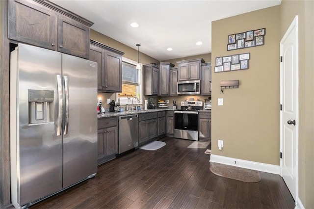 kitchen with a sink, dark brown cabinets, dark wood-style floors, appliances with stainless steel finishes, and decorative light fixtures