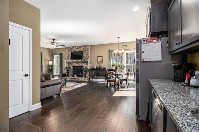 kitchen with open floor plan, a fireplace, dark brown cabinetry, dark wood-style flooring, and dark stone counters