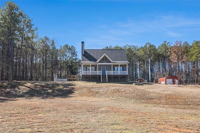 view of front of house with an outbuilding, a chimney, a garage, a front lawn, and covered porch