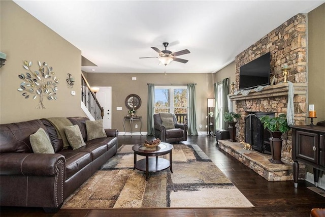 living room with dark wood-style floors, baseboards, a fireplace, ceiling fan, and stairs