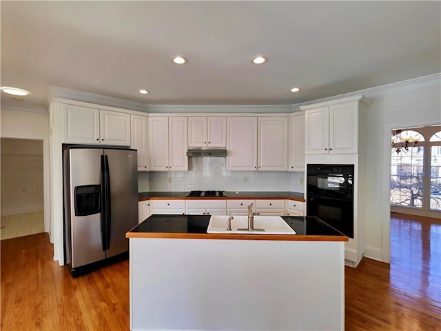 kitchen with dark countertops, black appliances, under cabinet range hood, and a sink