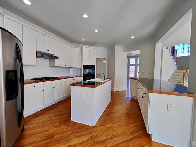 kitchen featuring under cabinet range hood, light wood-type flooring, black appliances, tasteful backsplash, and a center island with sink