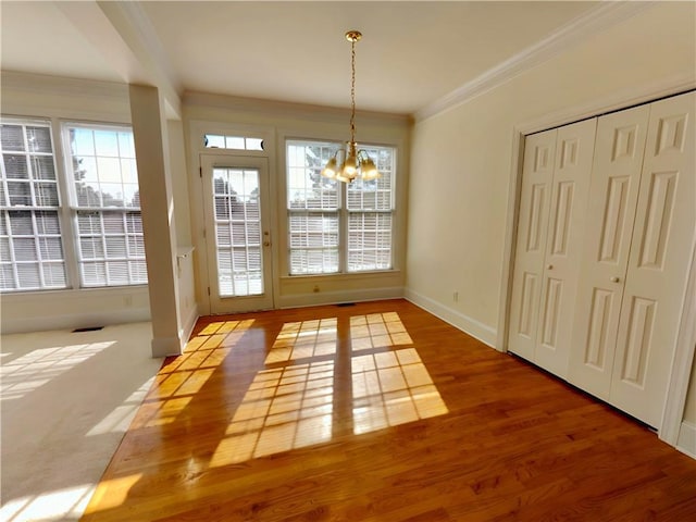 unfurnished dining area featuring a healthy amount of sunlight, an inviting chandelier, wood finished floors, and crown molding