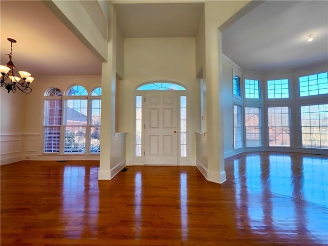 foyer featuring a chandelier, crown molding, wood finished floors, and a decorative wall