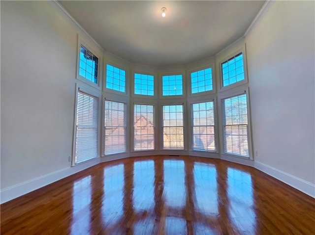 spare room featuring baseboards, wood finished floors, and crown molding