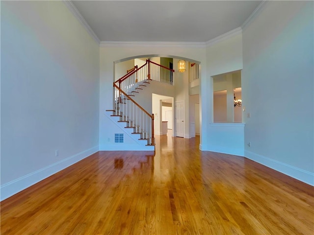 unfurnished living room with wood finished floors, visible vents, baseboards, stairs, and ornamental molding