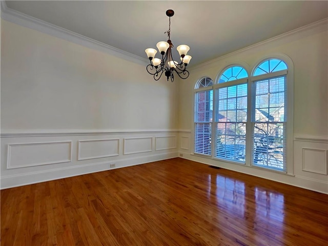 spare room with ornamental molding, wood finished floors, visible vents, and an inviting chandelier