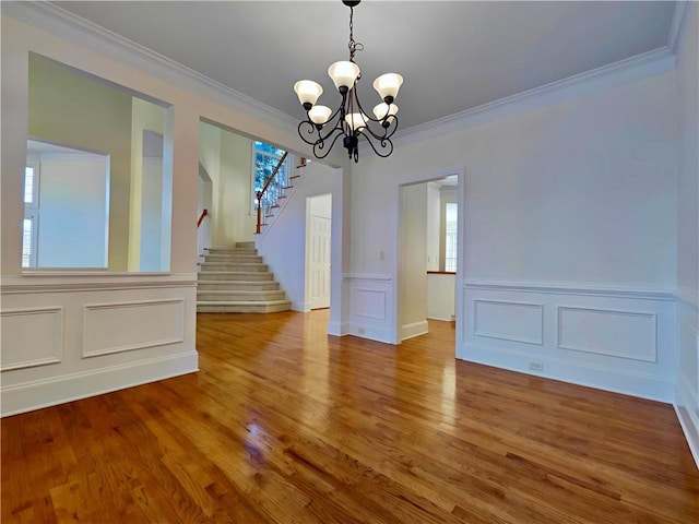 unfurnished dining area featuring a notable chandelier, crown molding, stairs, and wood finished floors