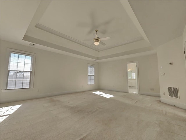 spare room featuring a raised ceiling, light colored carpet, visible vents, a ceiling fan, and baseboards