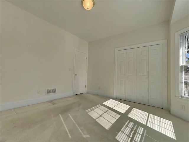 unfurnished bedroom featuring light carpet, a closet, visible vents, and baseboards