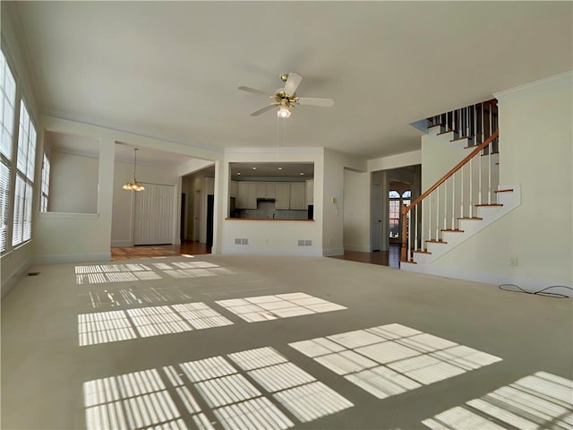 unfurnished living room featuring visible vents, stairs, baseboards, and ceiling fan with notable chandelier