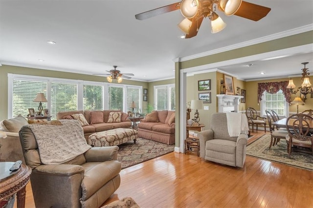 living room with crown molding, ceiling fan with notable chandelier, a wealth of natural light, and light hardwood / wood-style floors