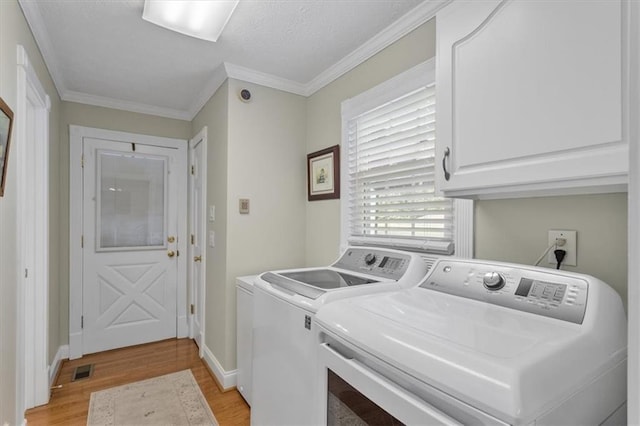 laundry room featuring ornamental molding, washing machine and dryer, cabinets, and light hardwood / wood-style flooring