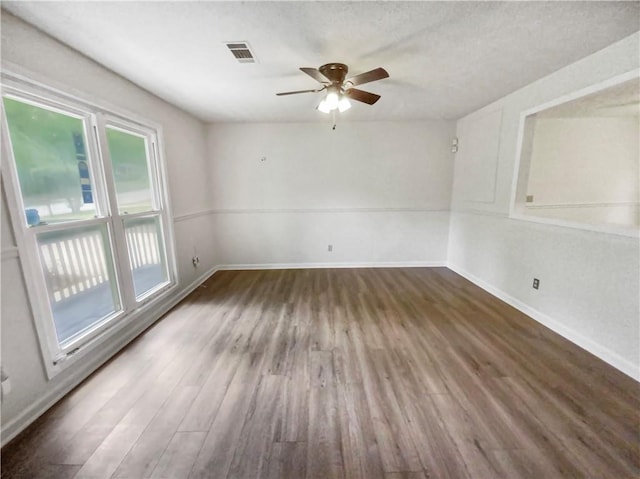 empty room featuring a wealth of natural light, wood finished floors, visible vents, and baseboards