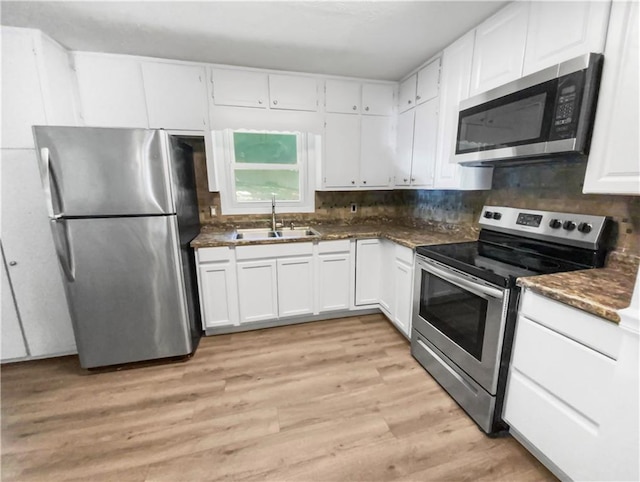 kitchen featuring decorative backsplash, white cabinets, appliances with stainless steel finishes, light wood-style floors, and a sink