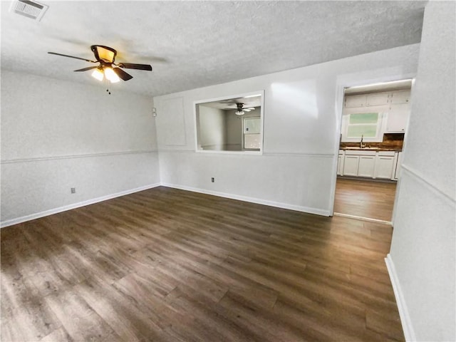 unfurnished room with a textured ceiling, dark wood-style flooring, a ceiling fan, visible vents, and baseboards