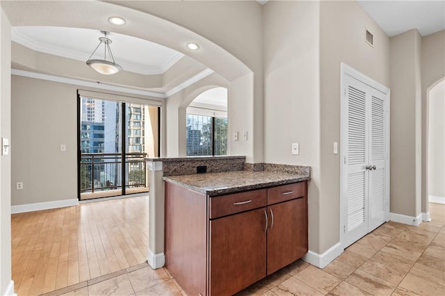 kitchen featuring kitchen peninsula, hanging light fixtures, dark stone counters, crown molding, and light hardwood / wood-style flooring