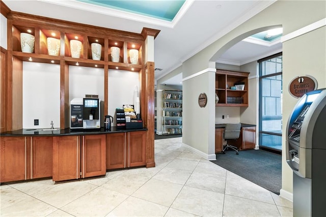 bar with light tile patterned flooring, crown molding, and built in desk