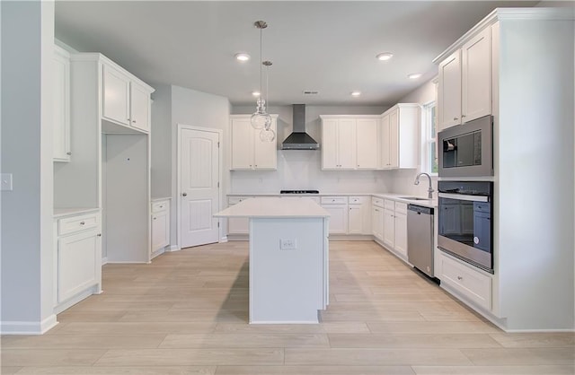 kitchen with stainless steel appliances, wall chimney exhaust hood, a sink, a center island, and light wood-type flooring