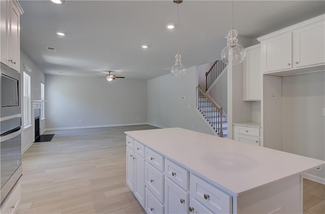kitchen with ceiling fan, light wood-style floors, light countertops, a center island, and white cabinetry
