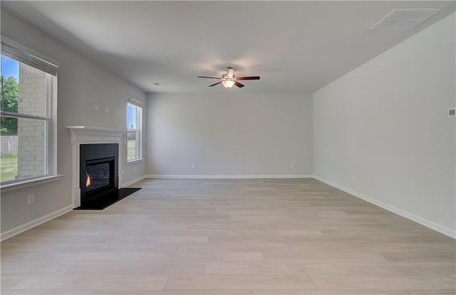 unfurnished living room with ceiling fan, a glass covered fireplace, light wood-style flooring, and baseboards