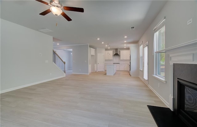 unfurnished living room with stairway, a high end fireplace, light wood-type flooring, ceiling fan, and recessed lighting