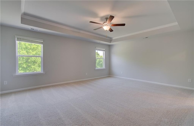 carpeted empty room with a raised ceiling, a ceiling fan, baseboards, and crown molding