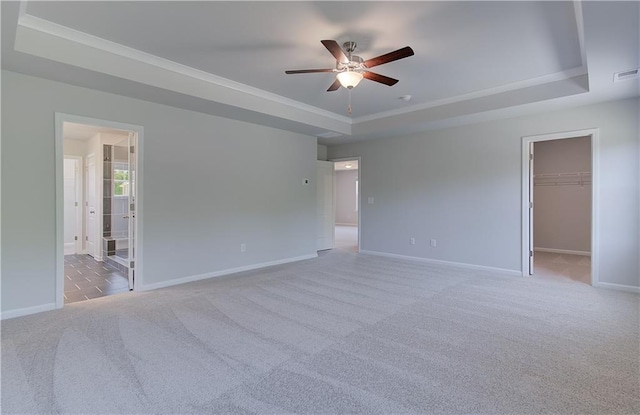 empty room with a tray ceiling, a ceiling fan, baseboards, light carpet, and ornamental molding