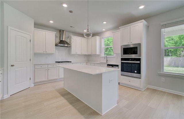 kitchen with appliances with stainless steel finishes, wall chimney exhaust hood, a sink, healthy amount of natural light, and recessed lighting