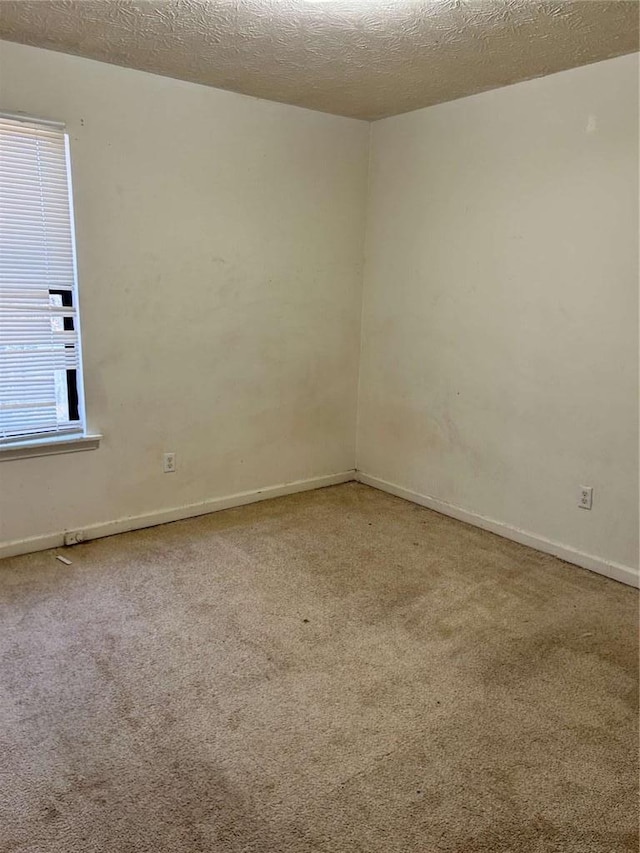 unfurnished room with a textured ceiling, carpet flooring, and baseboards