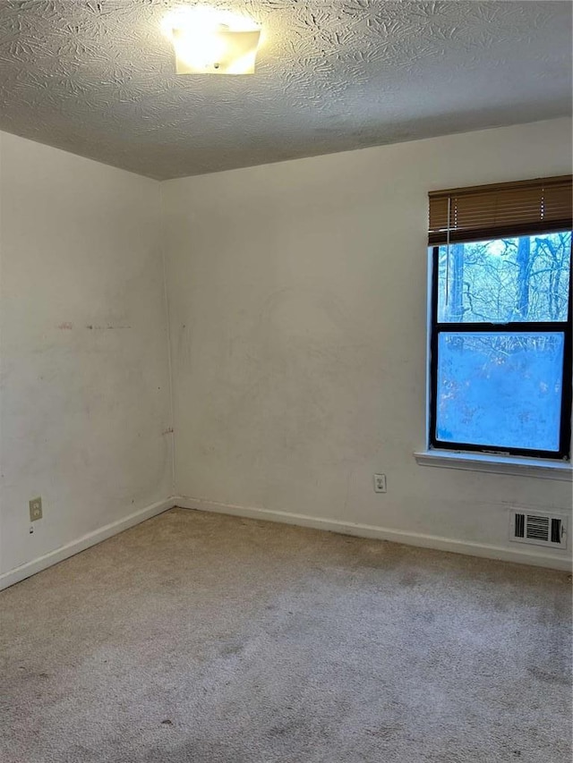 carpeted spare room featuring baseboards, visible vents, and a textured ceiling