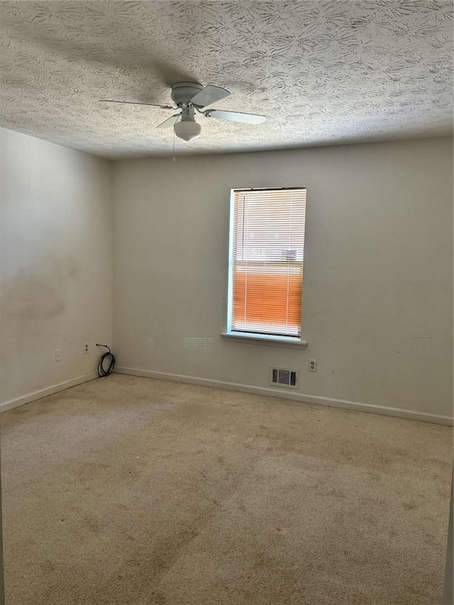 carpeted spare room featuring ceiling fan, a textured ceiling, visible vents, and baseboards