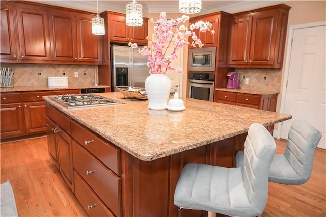 kitchen featuring decorative light fixtures, backsplash, a kitchen breakfast bar, light hardwood / wood-style floors, and stainless steel appliances