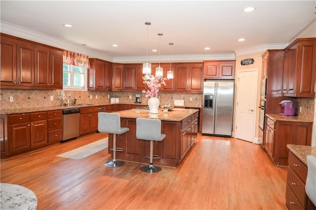 kitchen with decorative light fixtures, a kitchen breakfast bar, a kitchen island, stainless steel appliances, and light hardwood / wood-style floors