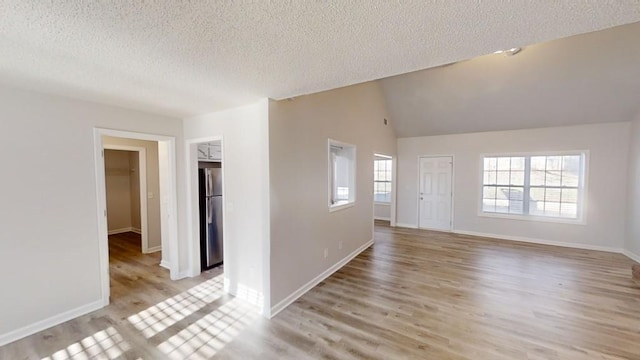 empty room with a healthy amount of sunlight, vaulted ceiling, light hardwood / wood-style flooring, and a textured ceiling