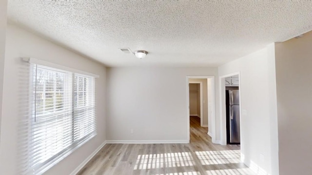 spare room featuring a textured ceiling and light hardwood / wood-style floors