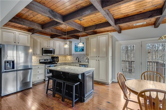 kitchen with sink, appliances with stainless steel finishes, backsplash, light stone countertops, and a kitchen island