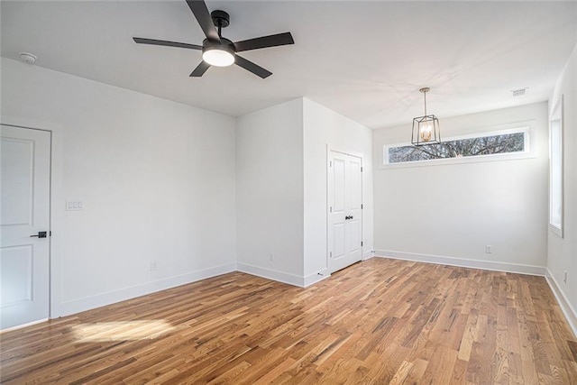 unfurnished room with ceiling fan with notable chandelier and wood-type flooring