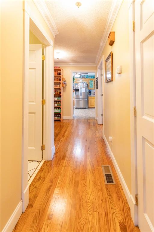 hall with a textured ceiling, light hardwood / wood-style flooring, and ornamental molding