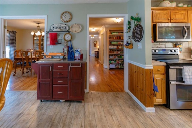 kitchen with appliances with stainless steel finishes, hanging light fixtures, light hardwood / wood-style floors, and an inviting chandelier