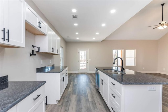 kitchen with sink, dark stone countertops, white cabinets, a center island with sink, and light hardwood / wood-style flooring