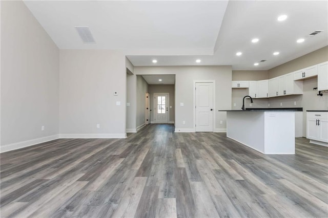 kitchen featuring wood-type flooring, sink, a kitchen island with sink, and white cabinets