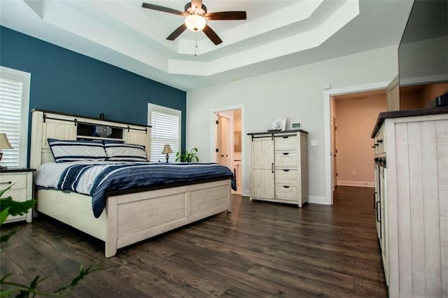 bedroom with a tray ceiling, dark wood-type flooring, connected bathroom, and ceiling fan