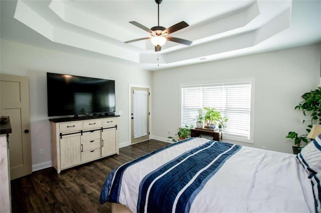 bedroom with dark hardwood / wood-style flooring, ceiling fan, and a tray ceiling